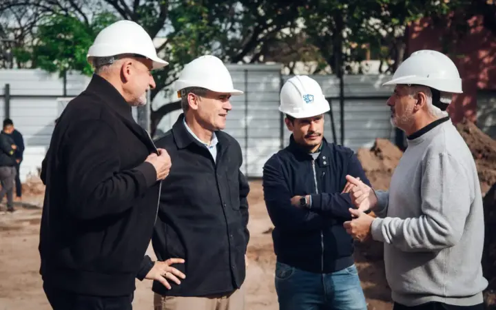 Cuatro hombres con casco blanco conversan en un terreno de obra durante la recorrida por el Paseo de las Artes